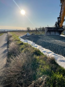 Baugrunduntersuchung in den Hochheimer Weinbergen. Das Bild zeigt links einen Weg an den rechts eine Wiese und Weinreben angrenzen. Eine Baggerschaufel arbeitet. Die Sonne scheint.