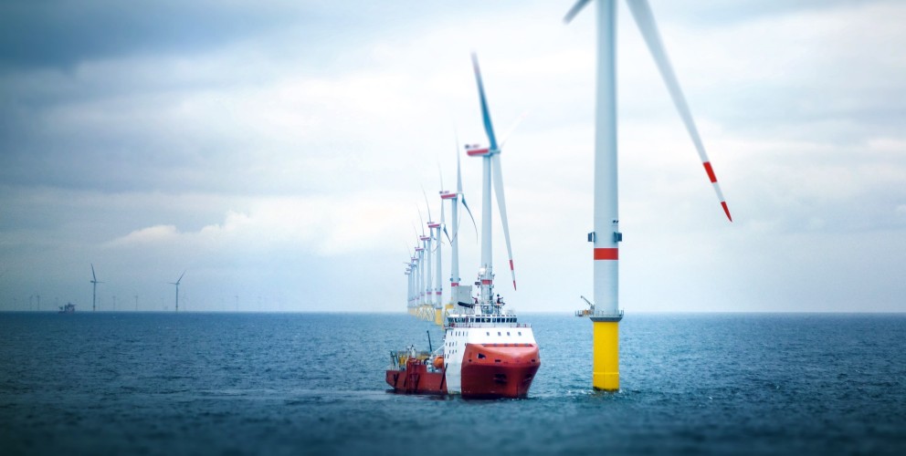 Offshore Windpark in der ruhigen Nordsee, im Vordergrund passiert ein rotes Schiff ein Windrad.